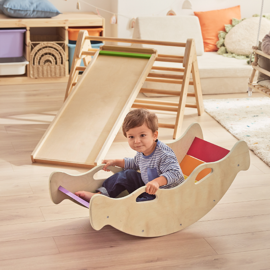 Toddler in a wooden rocking boat, with a wooden slide and climbing frame in the background.