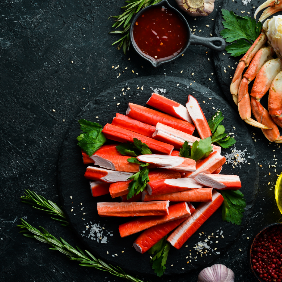 Crab sticks and crab claws on a dark slate background with herbs and spices.