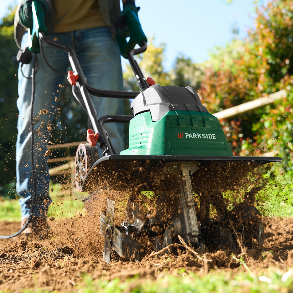 Person tilling soil with a green electric garden tiller, dirt flying up.
