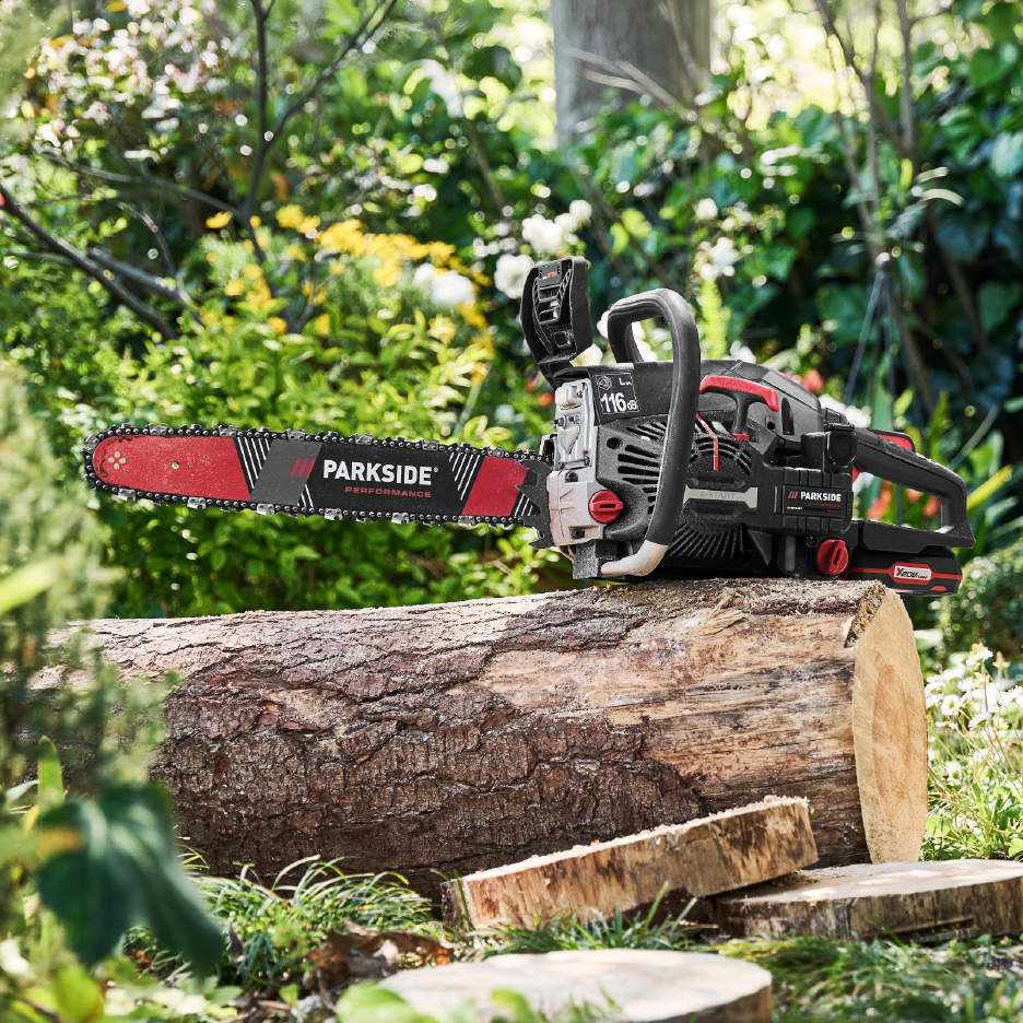 Cordless chainsaw on a cut log in a garden setting.
