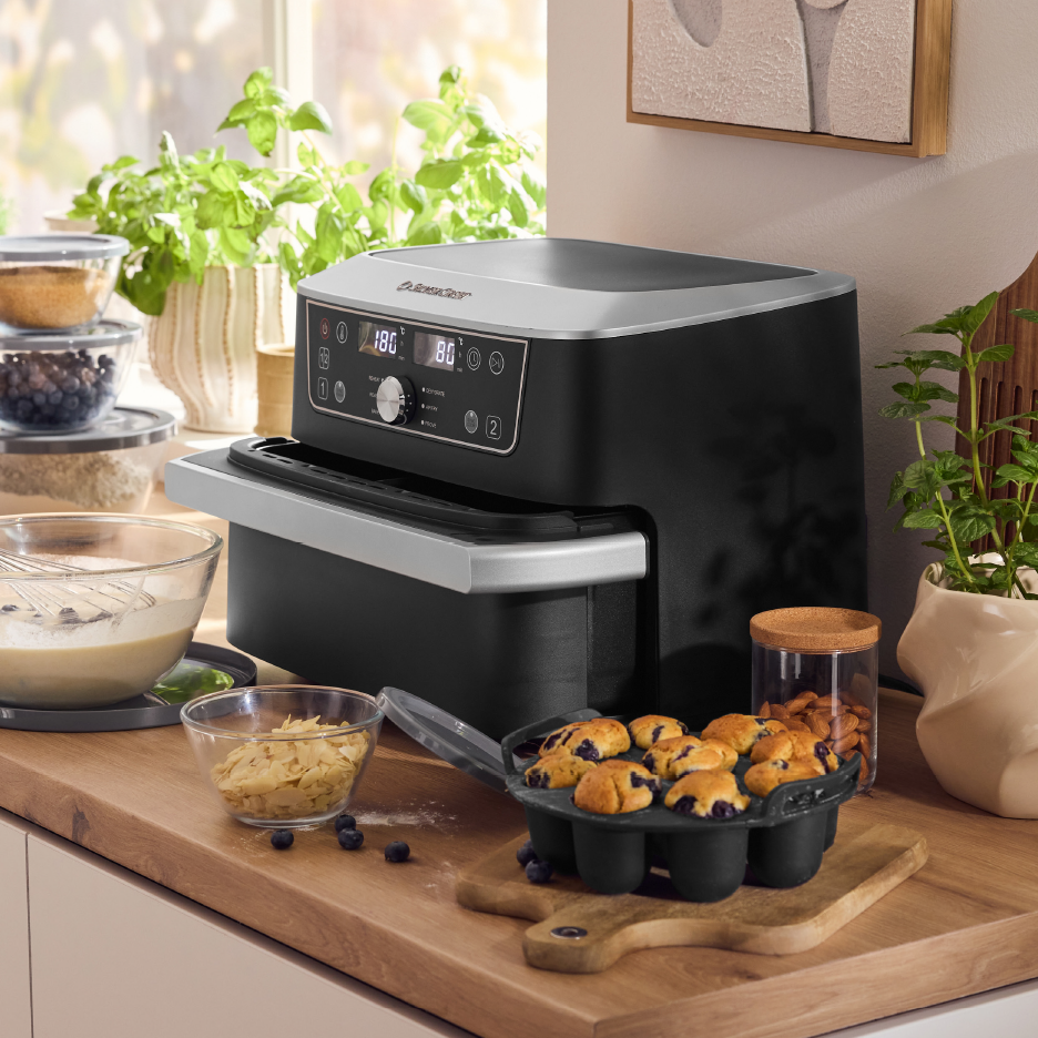 Φριτέζα αέρος σε πάγκο κουζίνας με υλικά ψησίματος και μάφινς με μύρτιλα.