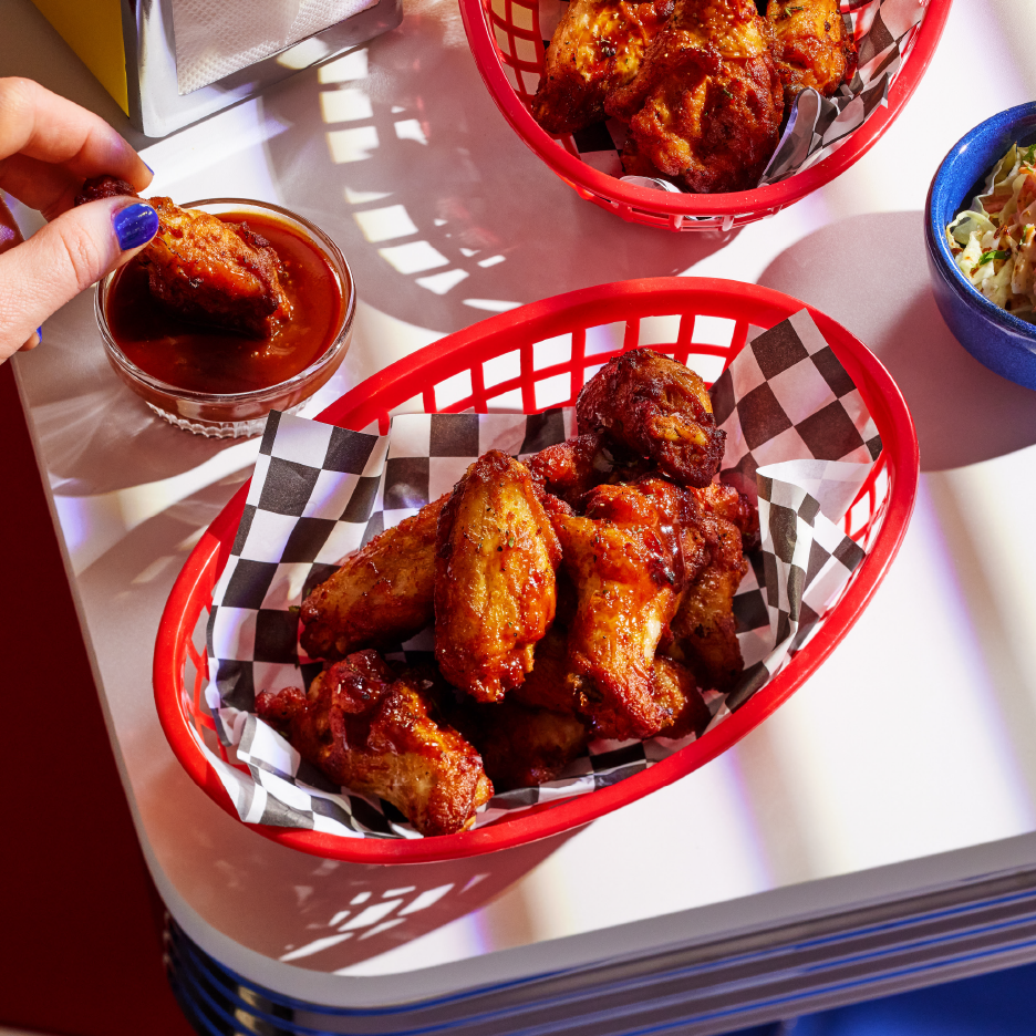 Φτερούγες κοτόπουλου σε κόκκινα καλάθια με καρό χαρτί, σάλτσα και λάχανο σαλάτα.