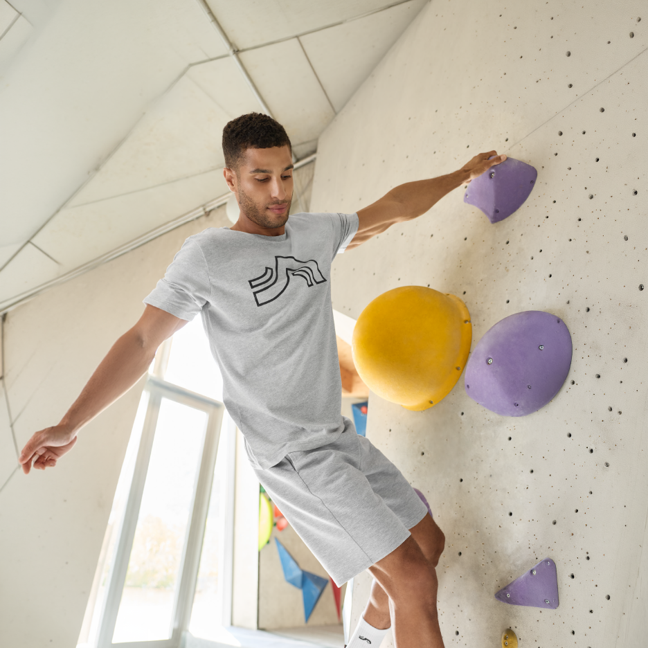 Άνδρας με γκρι μπλουζάκι και σορτς κάνει bouldering σε τοίχο αναρρίχησης.