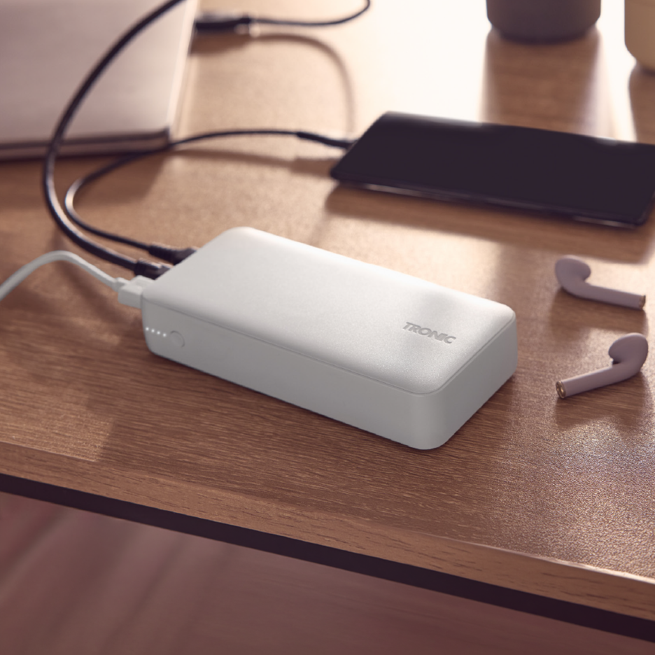 Λευκό power bank φορτίζει smartphone και laptop, με ασύρματα ακουστικά κοντά.