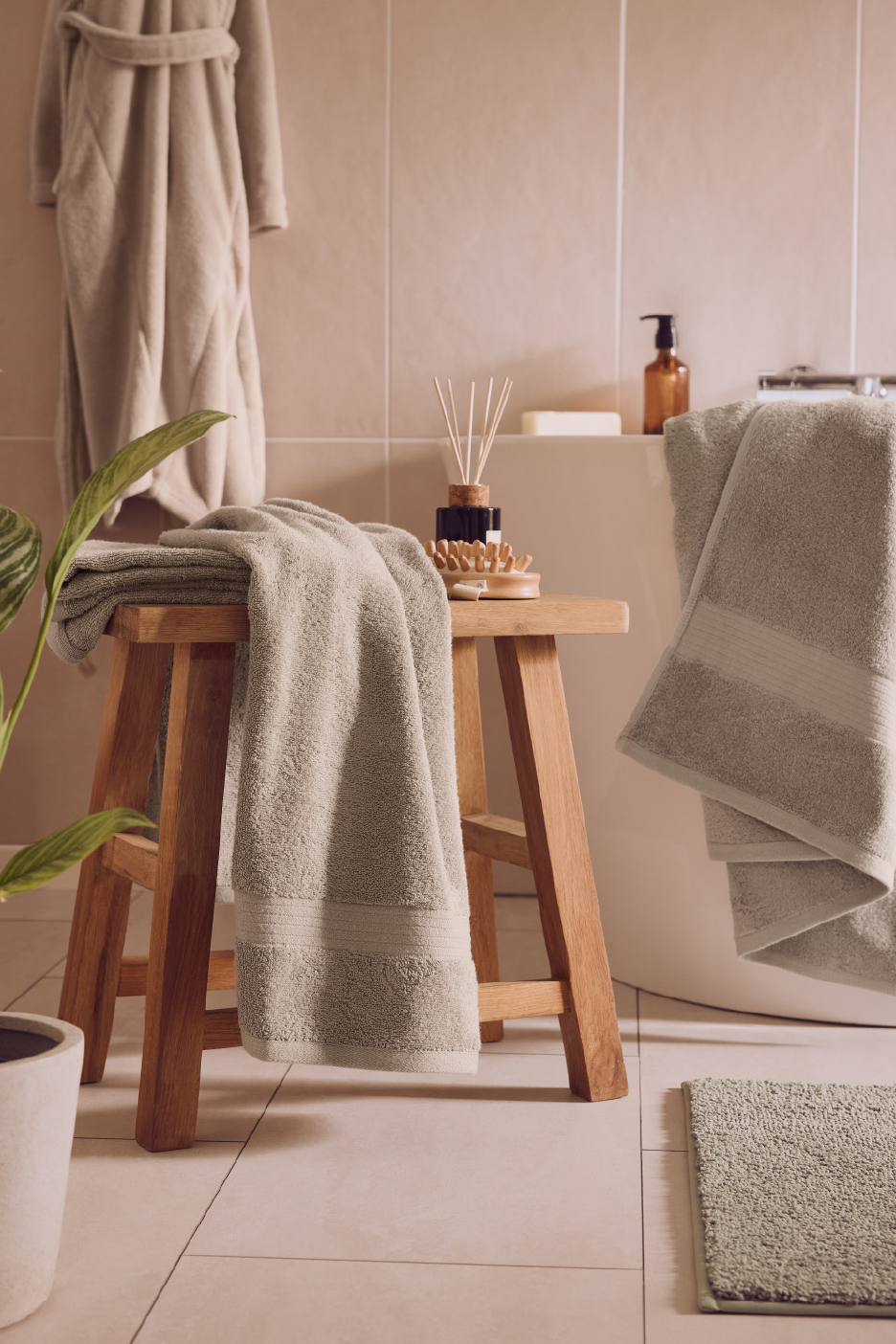 Μπάνιο με μπεζ πετσέτες, ξύλινο σκαμπό και φυτό, δημιουργώντας μια ατμόσφαιρα σπα.