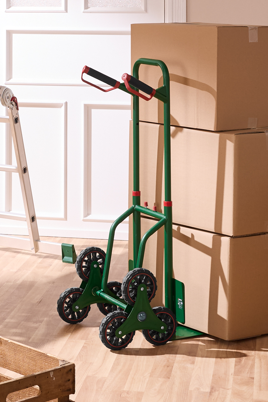 Πράσινο καρότσι σκάλας με κούτες μετακόμισης και μια σκάλα σε ένα δωμάτιο.