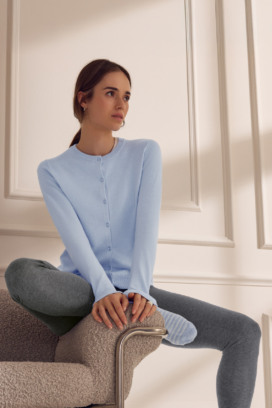 Γυναίκα με γαλάζια ζακέτα και γκρι κολάν κάθεται σε καρέκλα