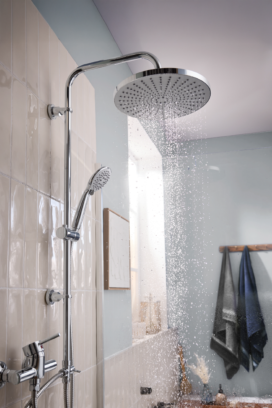 Chrome shower system with a large overhead shower and a handheld shower, water running.