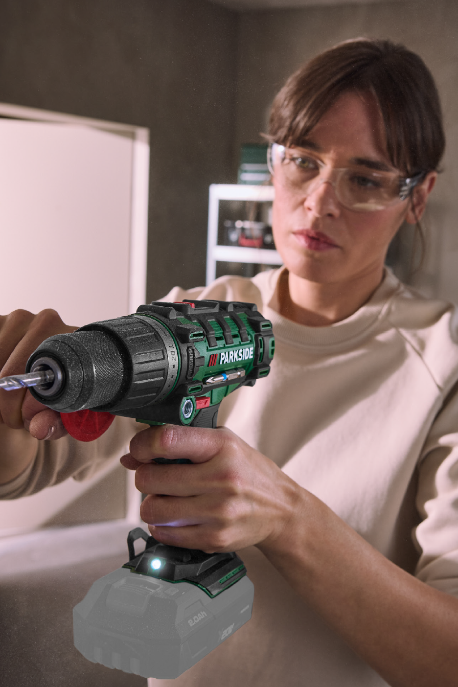 Γυναίκα με γυαλιά ασφαλείας κρατάει ένα ασύρματο δράπανο με μπαταρία, έτοιμη για εργασία.