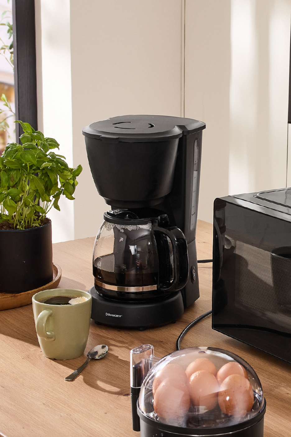Coffee maker and microwave on a kitchen counter with a basil plant and spices.