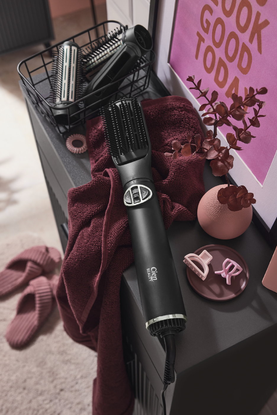 Hair styling brush and accessories on a dark surface with a burgundy towel.