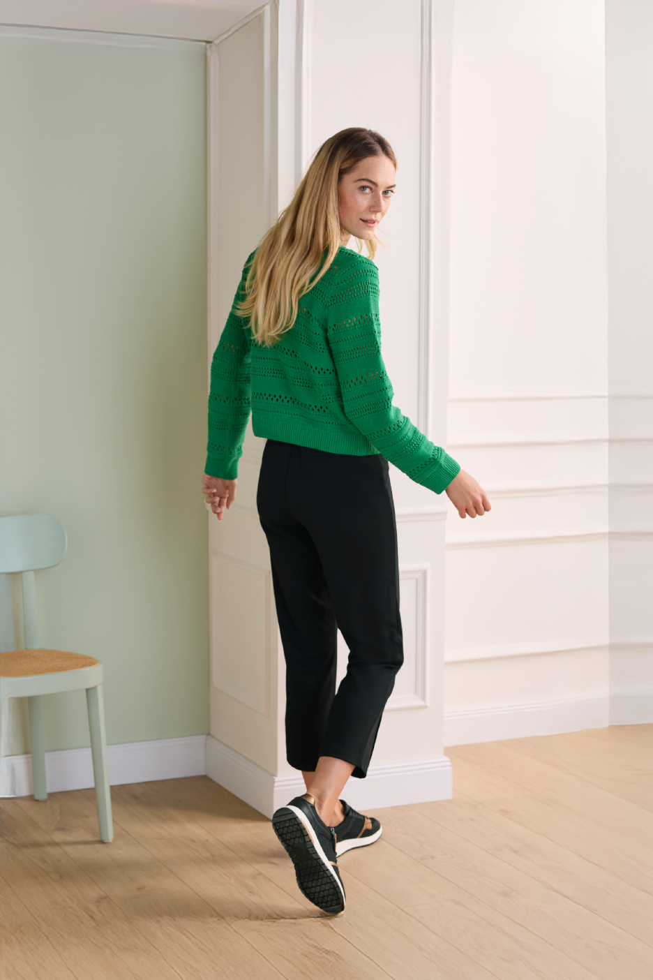 Γυναίκα με πράσινο πλεκτό πουλόβερ, μαύρο παντελόνι και μαύρα αθλητικά, κοιτάζει πίσω.