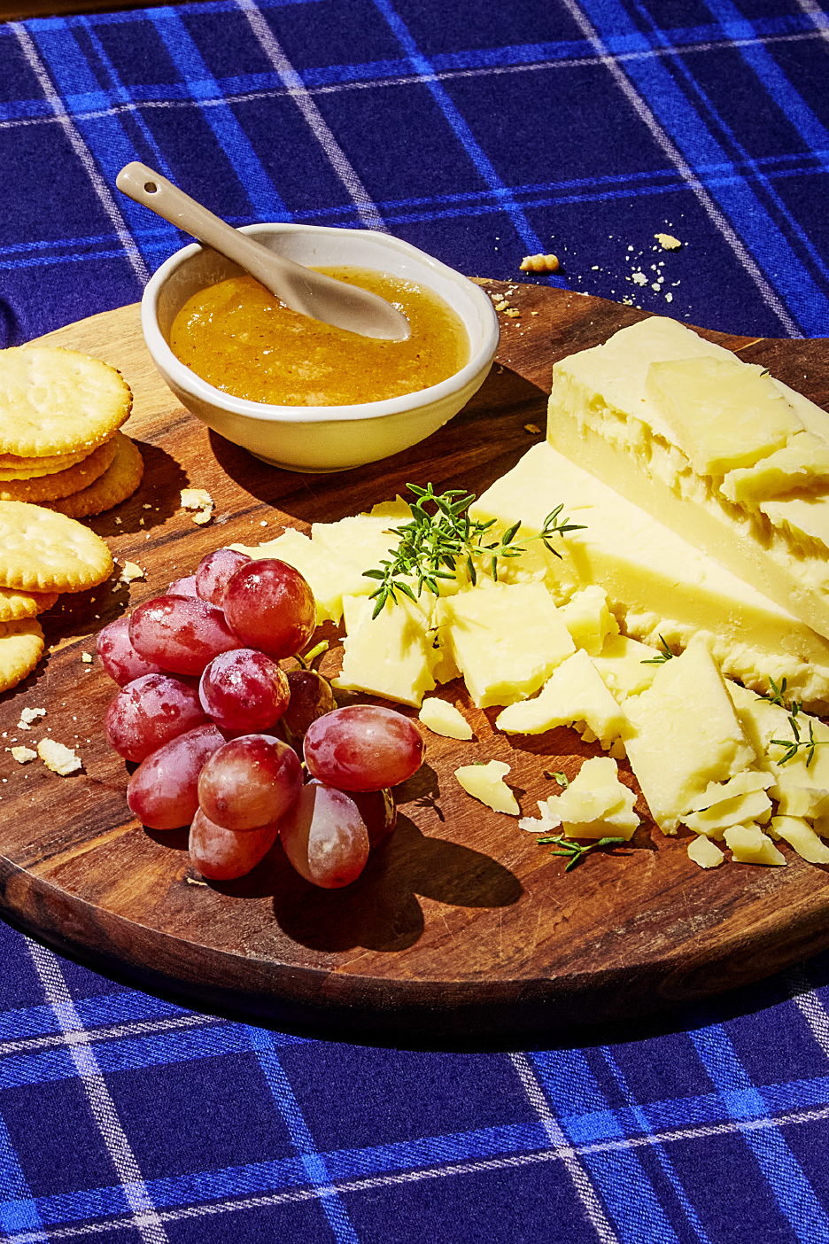 Πιατέλα τυριών με κράκερ, σταφύλια και μαρμελάδα σε μπλε καρό κουβέρτα.