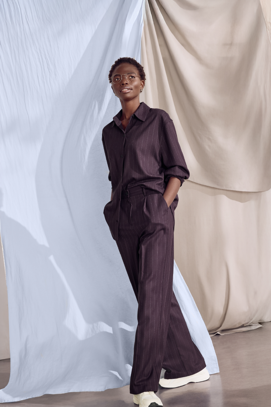 Γυναίκα με σκούρο ριγέ πουκάμισο και ασορτί παντελόνι, με λευκά αθλητικά.