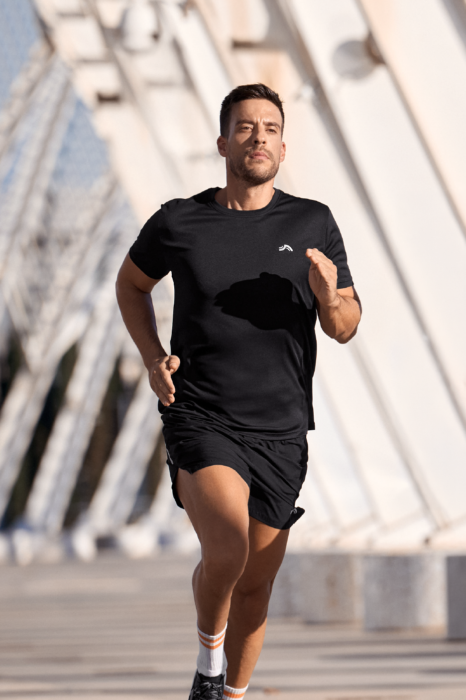 Άνδρας τρέχει με μαύρο αθλητικό μπλουζάκι και σορτς με λευκές ριγέ κάλτσες.