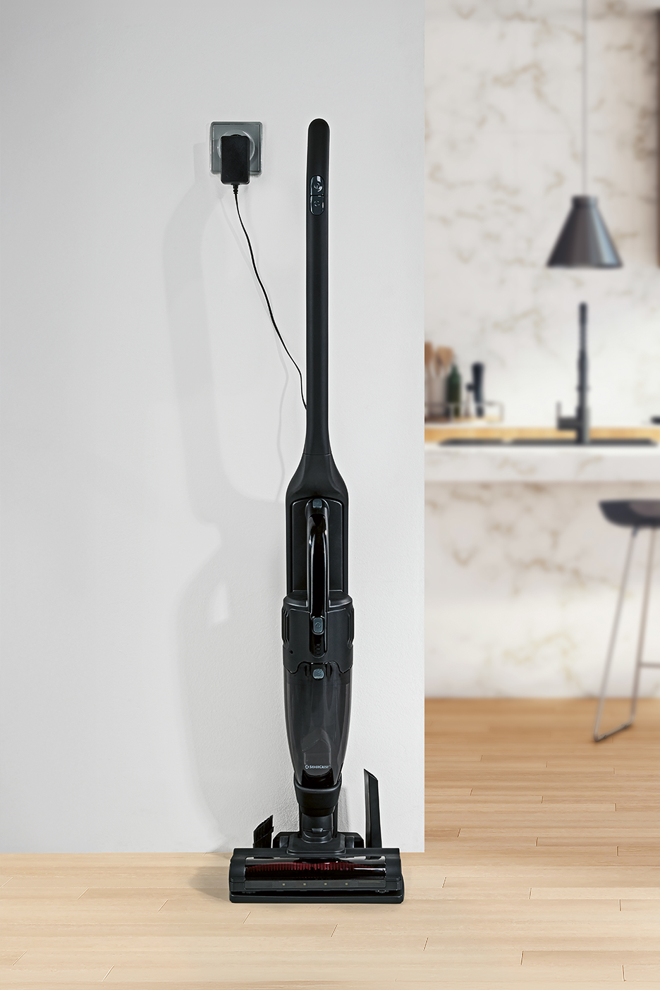 Ασύρματη ηλεκτρική σκούπα stick φορτίζει σε λευκό τοίχο σε μια μοντέρνα κουζίνα.