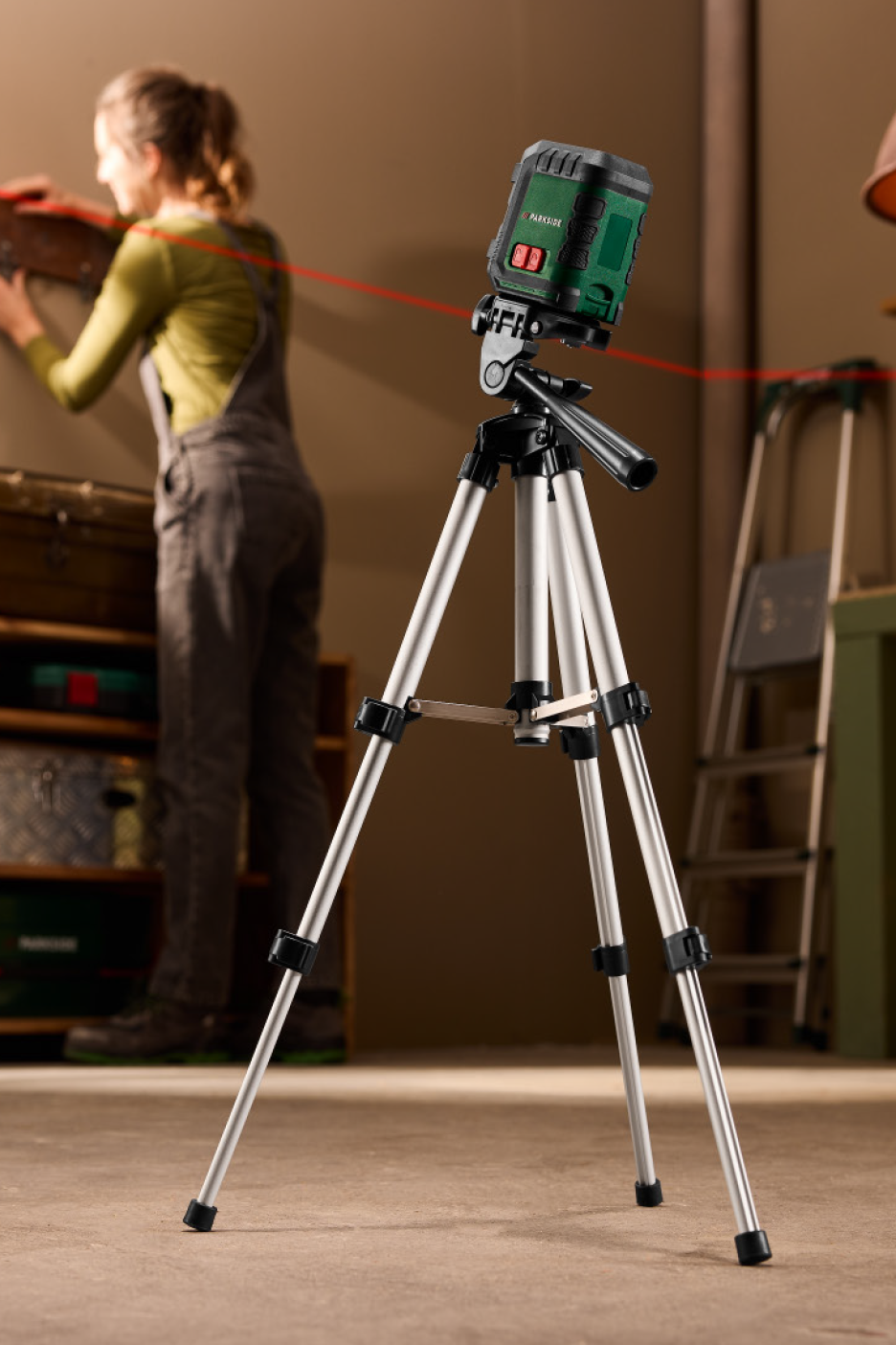 Αλφάδι λέιζερ σε τρίποδο, που προβάλλει μια κόκκινη γραμμή, με ένα άτομο να εργάζεται στο παρασκήνιο.