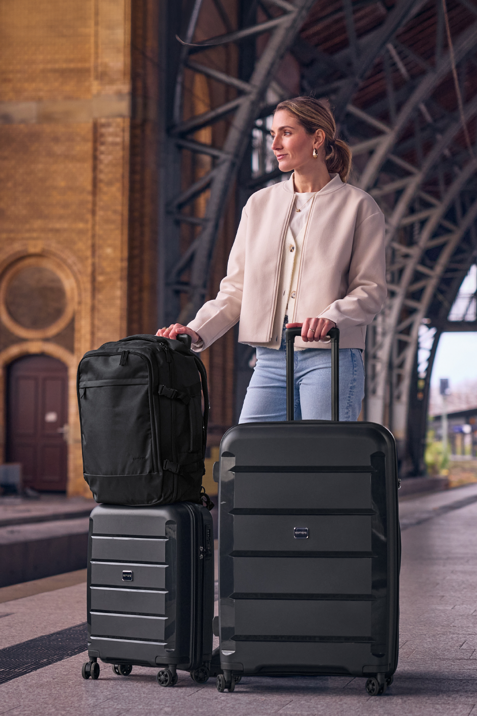 Γυναίκα με μαύρες αποσκευές και σακίδιο σε σιδηροδρομικό σταθμό.