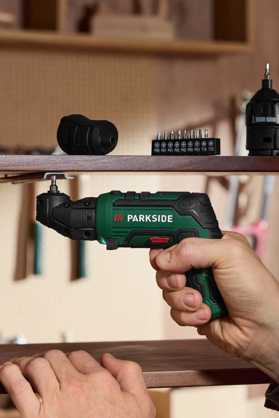Cordless screwdriver with an angled attachment, driving a screw into a wooden shelf.