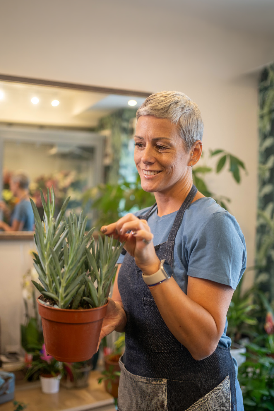 Woman in an apron holding a potted succulent plant in a store.