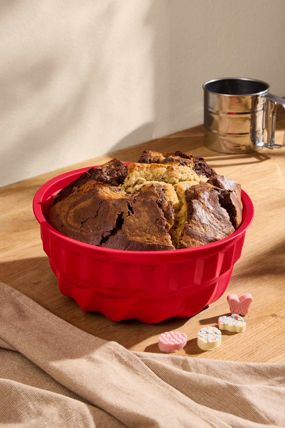 Μαρμπλ κέικ σε κόκκινη φόρμα σιλικόνης σε ξύλινο τραπέζι με κόσκινο αλευριού.