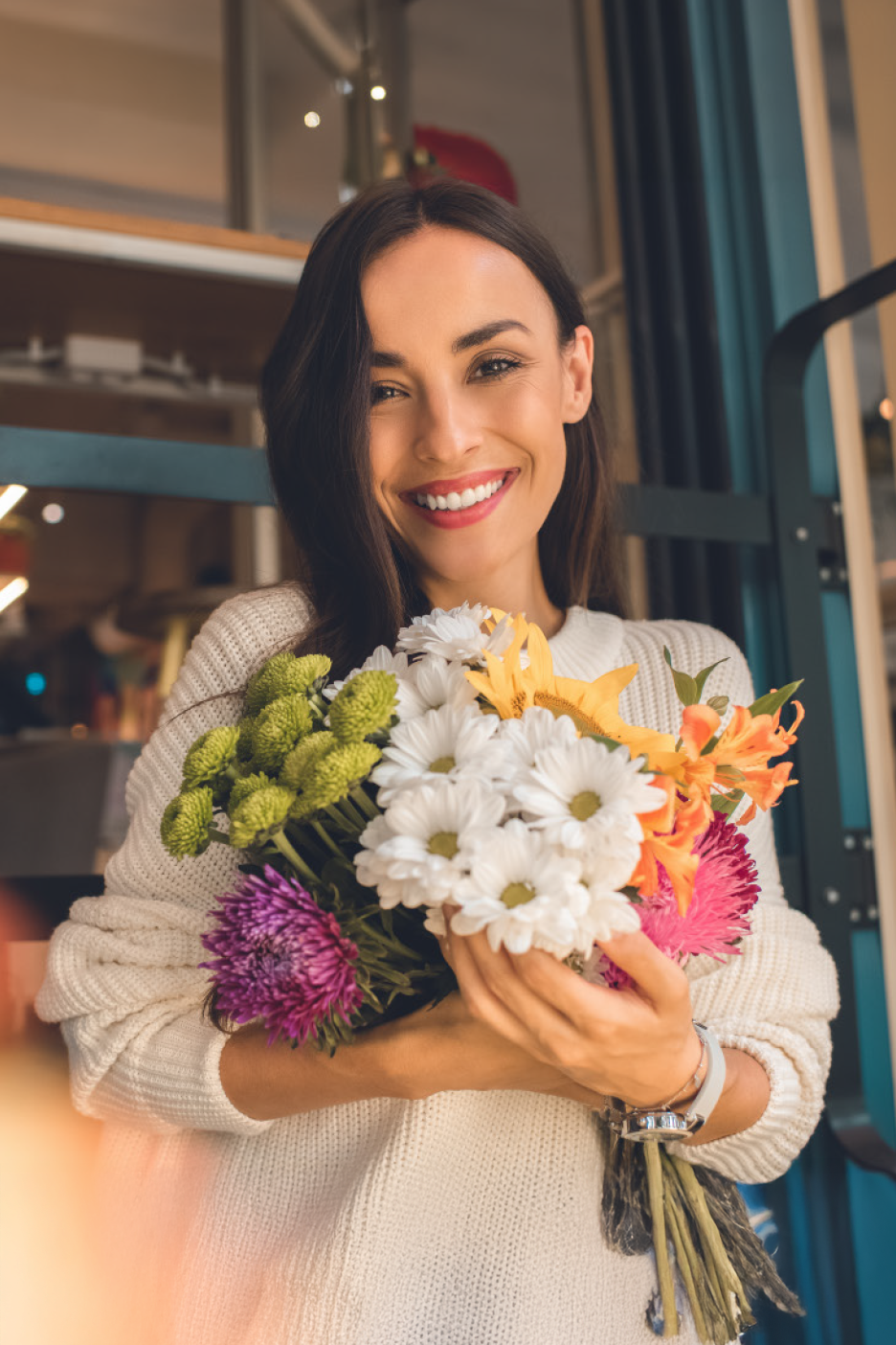 Χαμογελαστή γυναίκα κρατάει ένα ζωντανό μπουκέτο φρέσκων λουλουδιών, με λευκές μαργαρίτες και πράσινα χρυσάνθεμα.