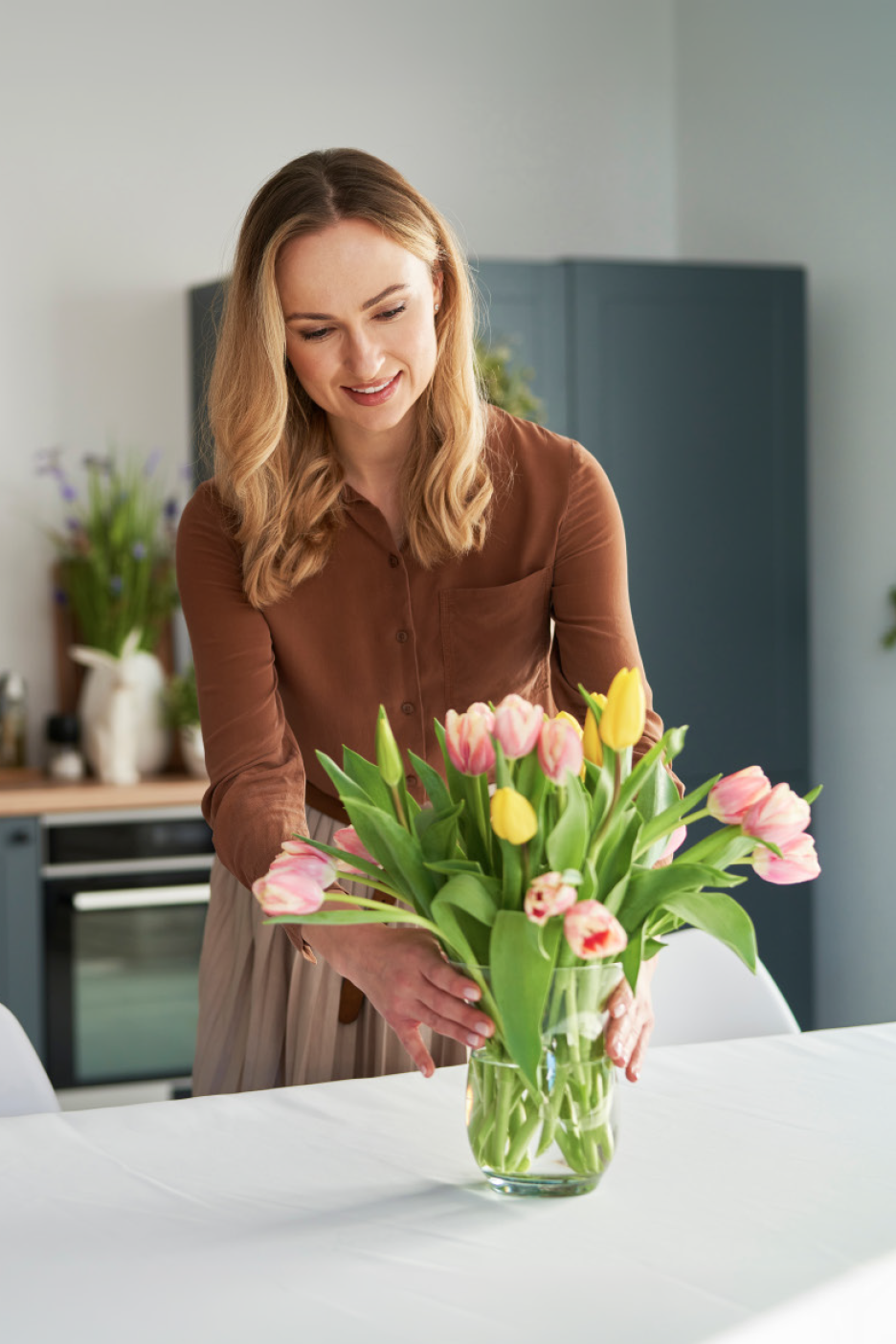 Γυναίκα τακτοποιεί ένα βάζο με ροζ και κίτρινες τουλίπες σε ένα λευκό τραπέζι.