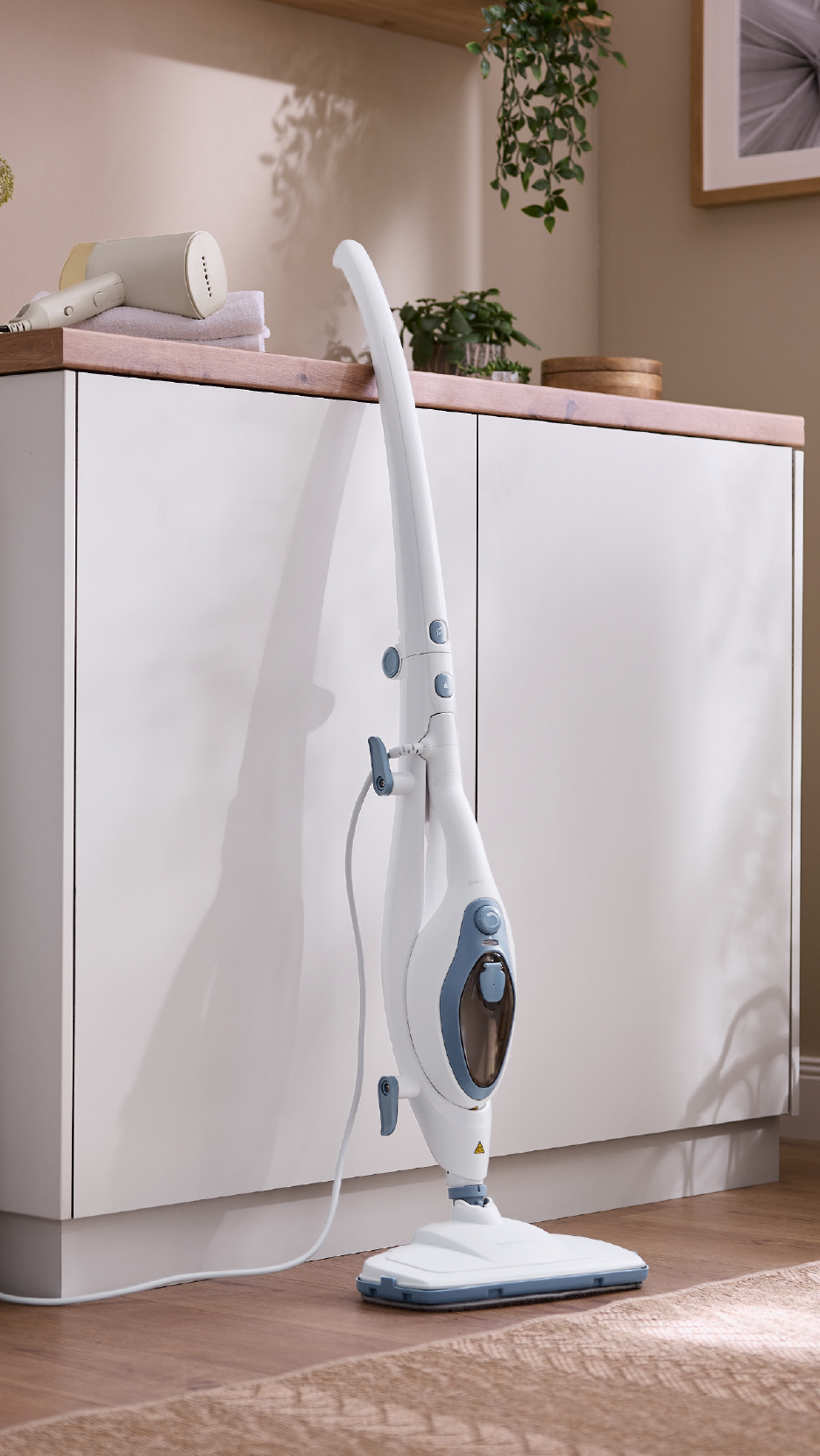 A white steam mop stands in a laundry room next to a washing machine and cabinets.