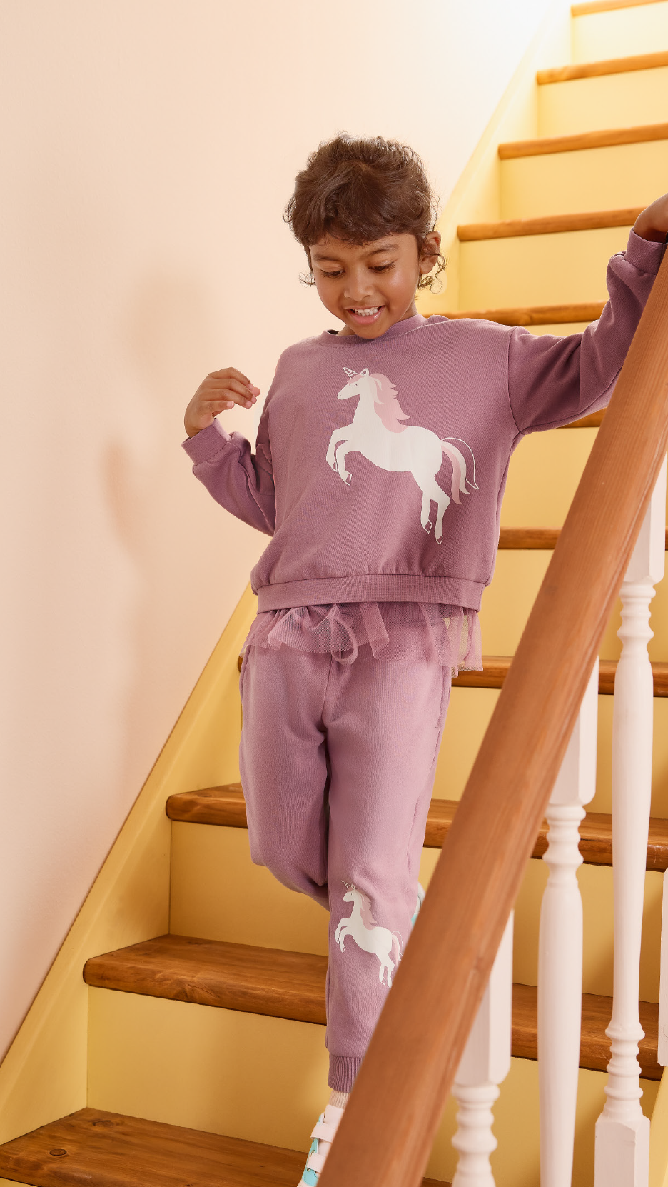 Girl in a purple unicorn sweatshirt and matching trousers on stairs.