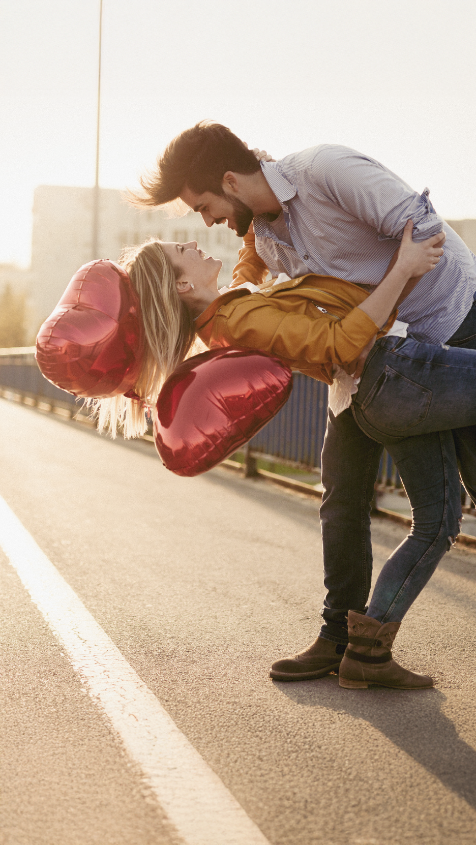 Couple in love on a bridge, holding heart-shaped balloons.