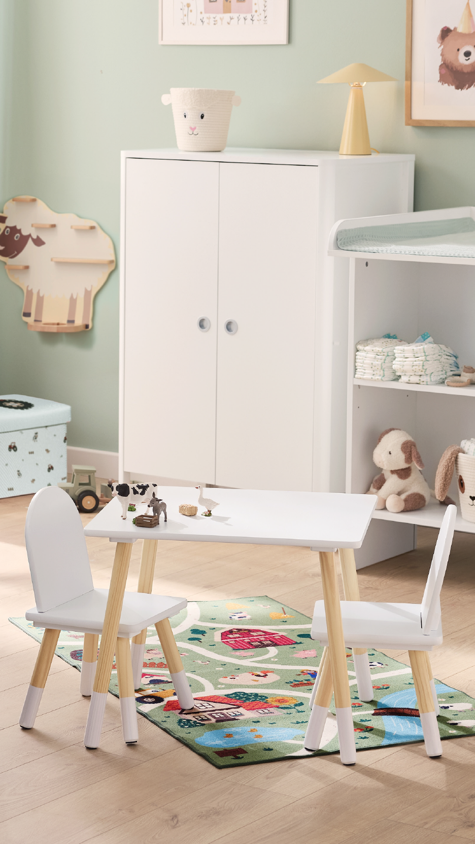 Παιδικό δωμάτιο με λευκό τραπέζι και καρέκλες, χαλί με φάρμα και έπιπλα αποθήκευσης.