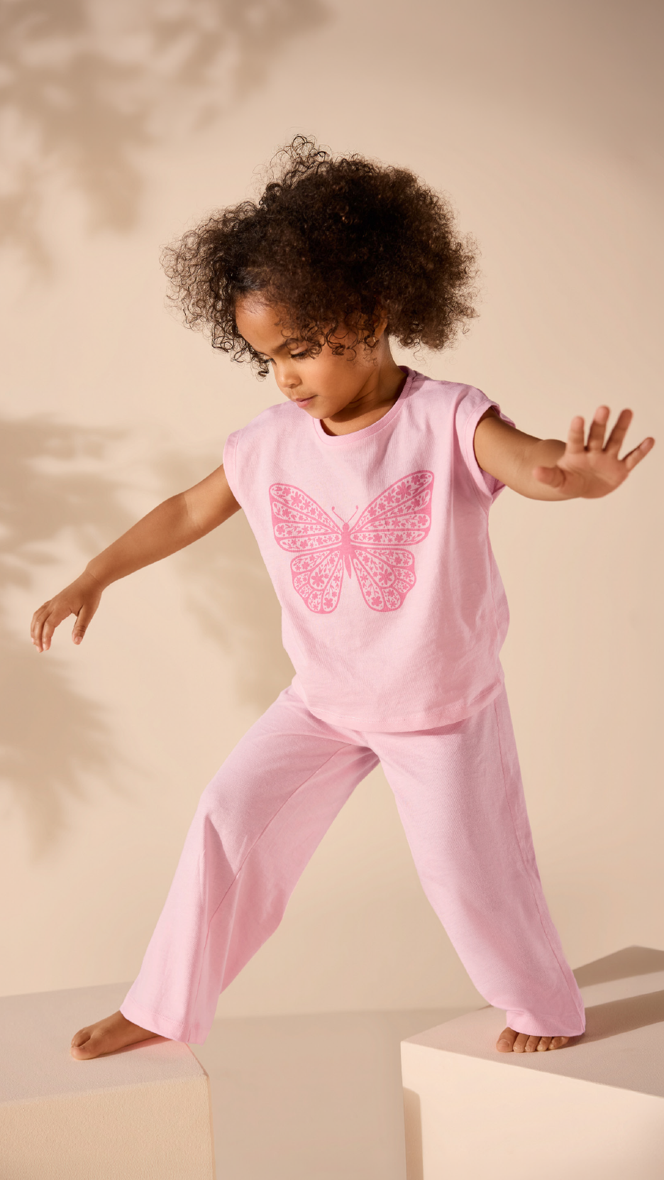 Young girl in a pink butterfly print t-shirt and matching trousers, reaching out.