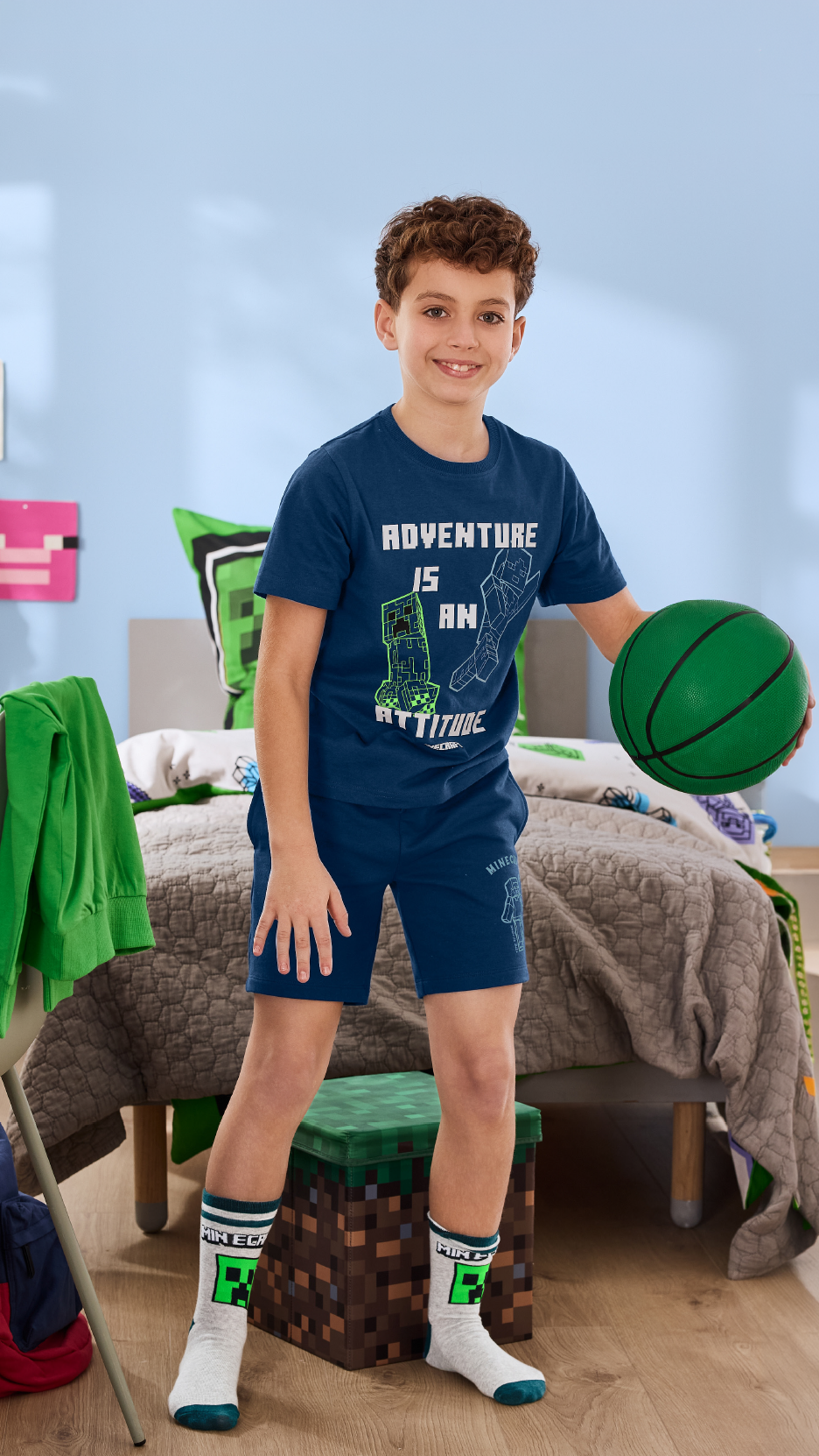 Αγόρι με μπλε μπλουζάκι και σορτς κρατώντας μια πράσινη μπάλα μπάσκετ, σε δωμάτιο με θέμα Minecraft.