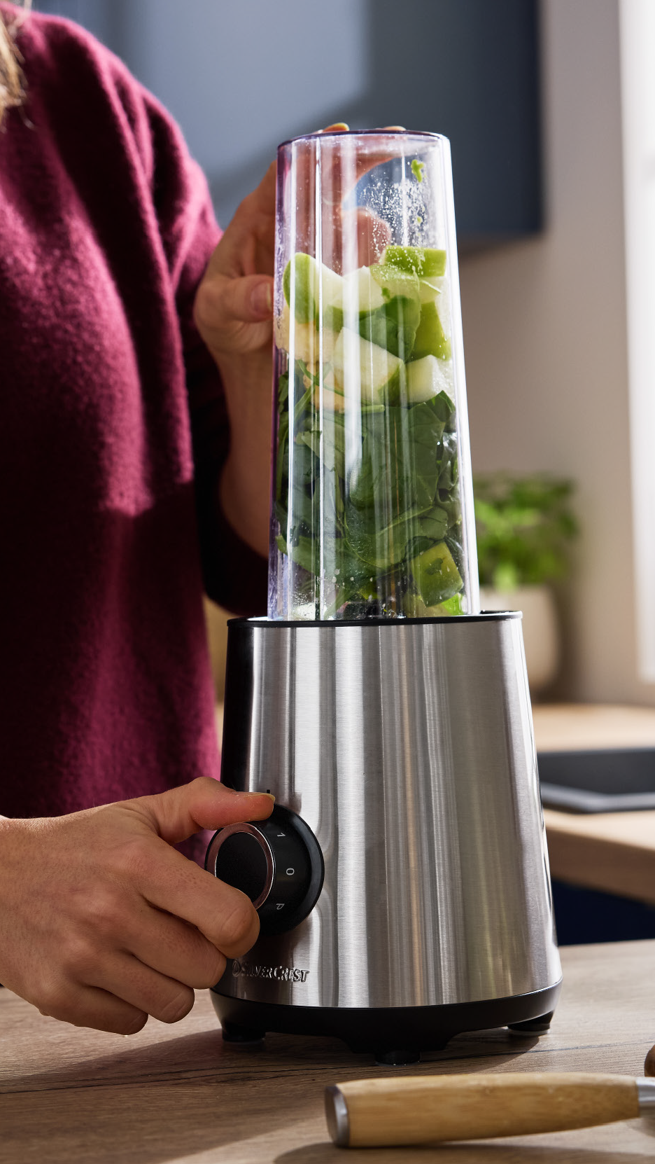 Άτομο που ετοιμάζει ένα πράσινο smoothie σε ένα μπλέντερ με βάση από ανοξείδωτο ατσάλι.