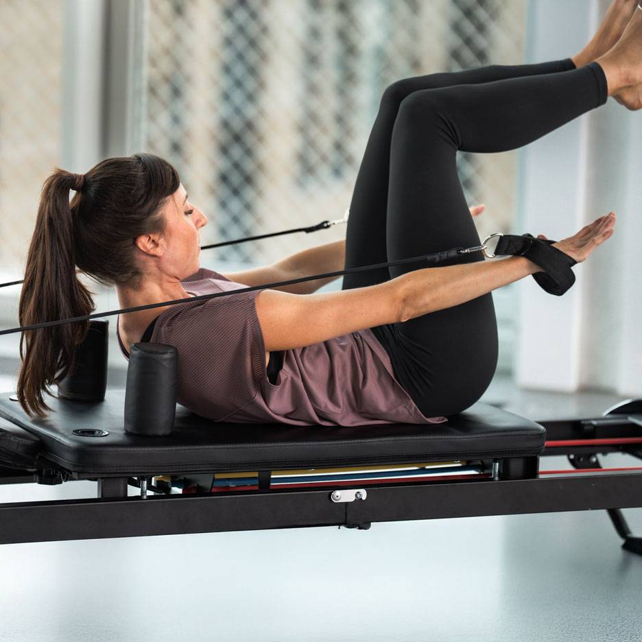 Woman exercising Pilates on a reformer, wearing black activewear.