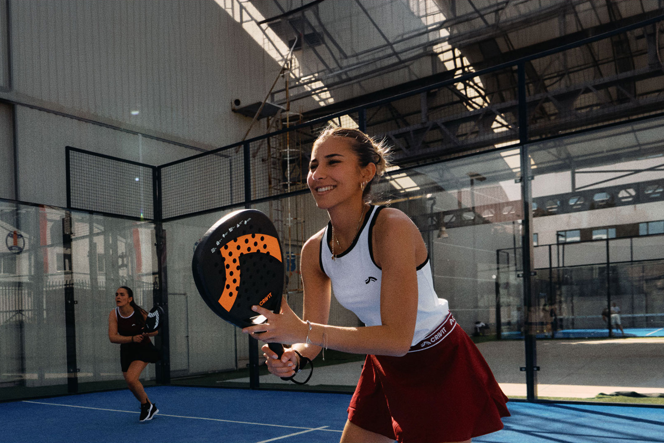 AI generated image: Two women playing padel tennis, one smiling and holding a racket, on a blue court.