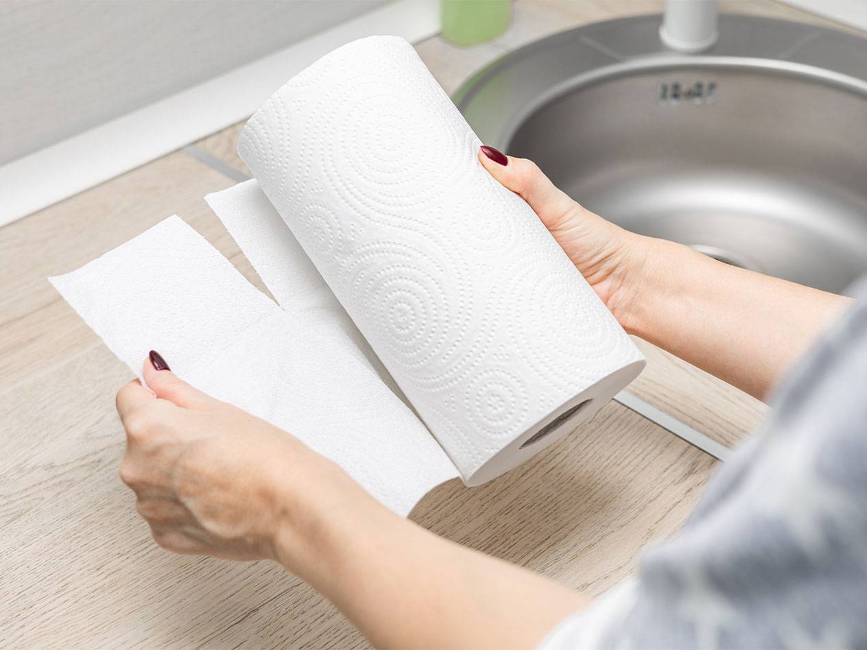 A person tears a paper towel from a roll next to a kitchen sink.
