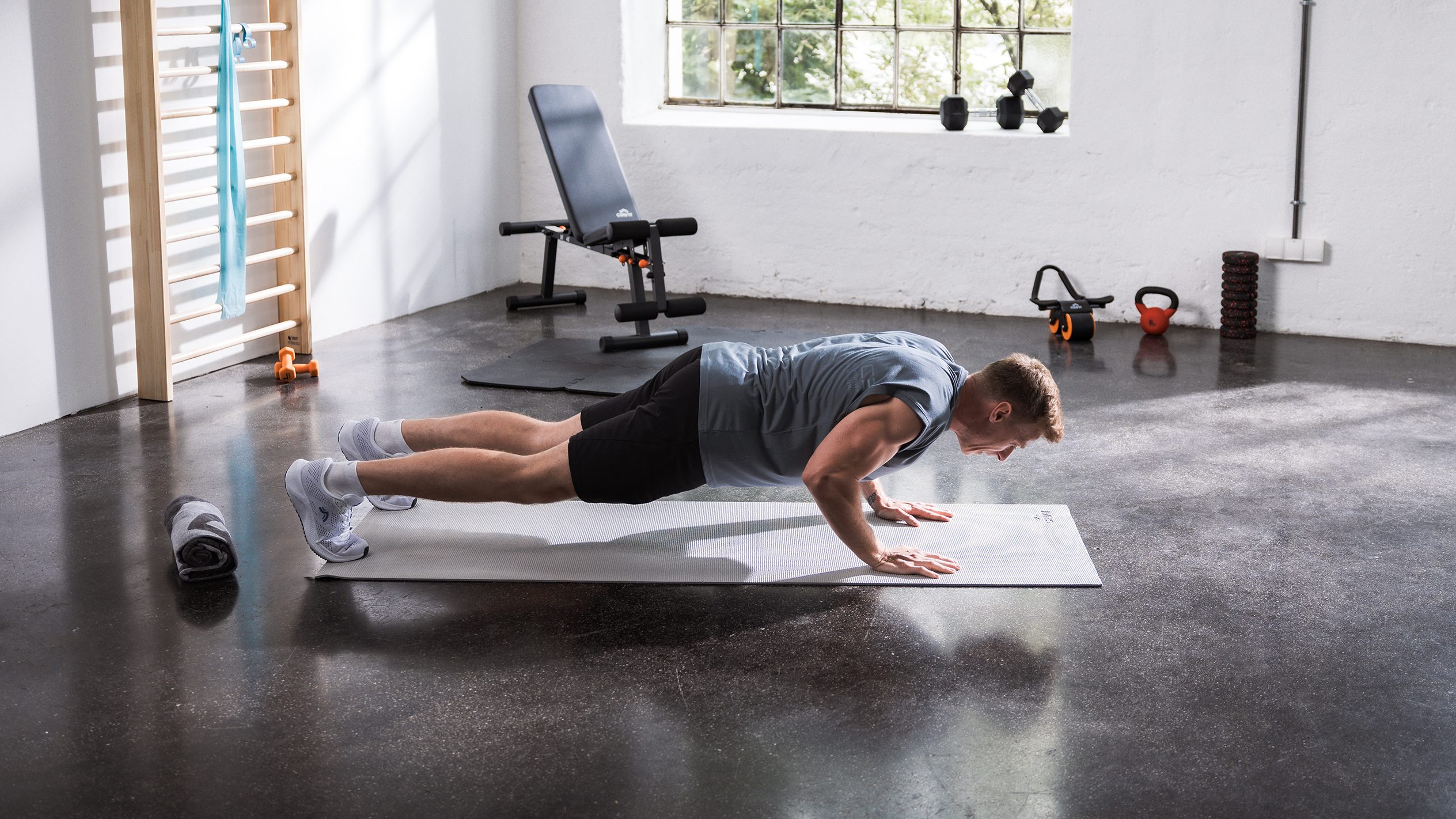 Man doing push-ups on a mat in a home gym with various fitness equipment.