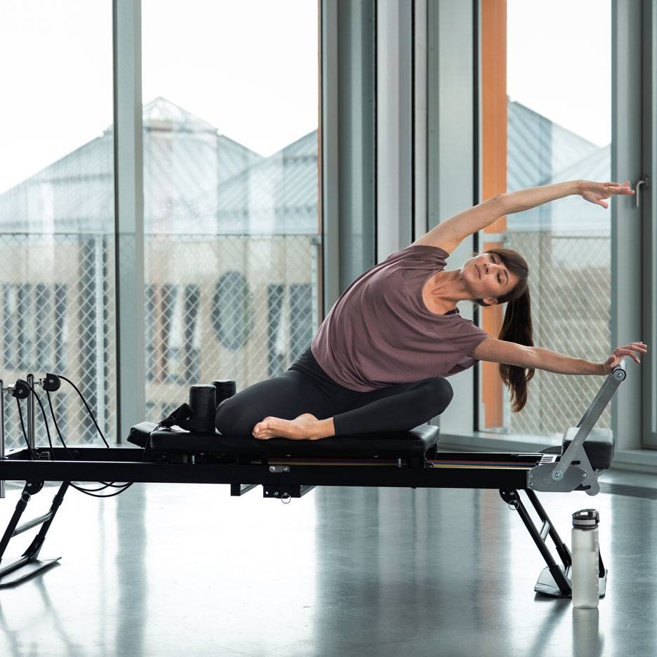 Woman doing Pilates on a reformer machine, stretching sideways.