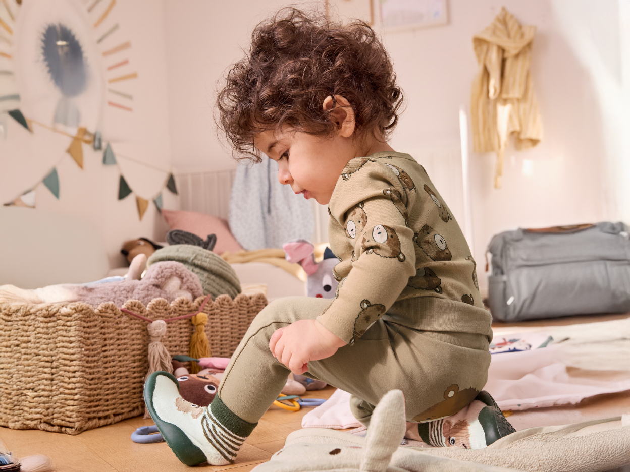 A baby in bear-patterned pajamas plays on the nursery floor.