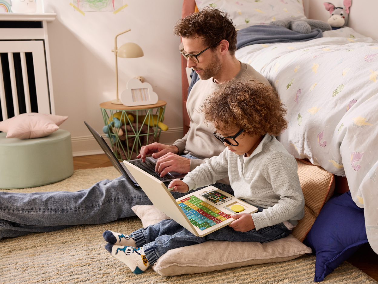 Father and child using laptops in a child's bedroom.