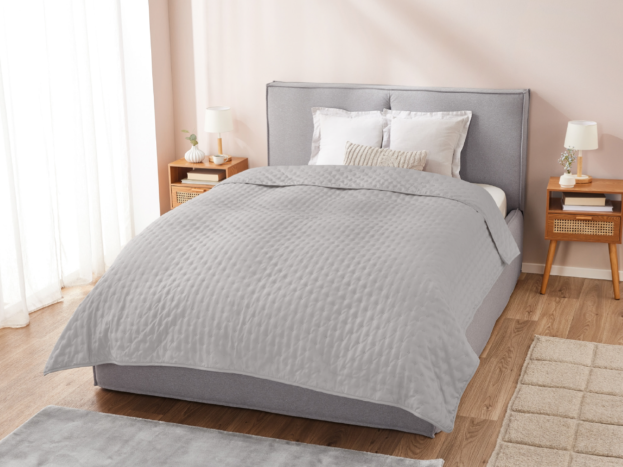 A modern bedroom with a grey upholstered bed, light grey quilted bedding, and wooden nightstands.