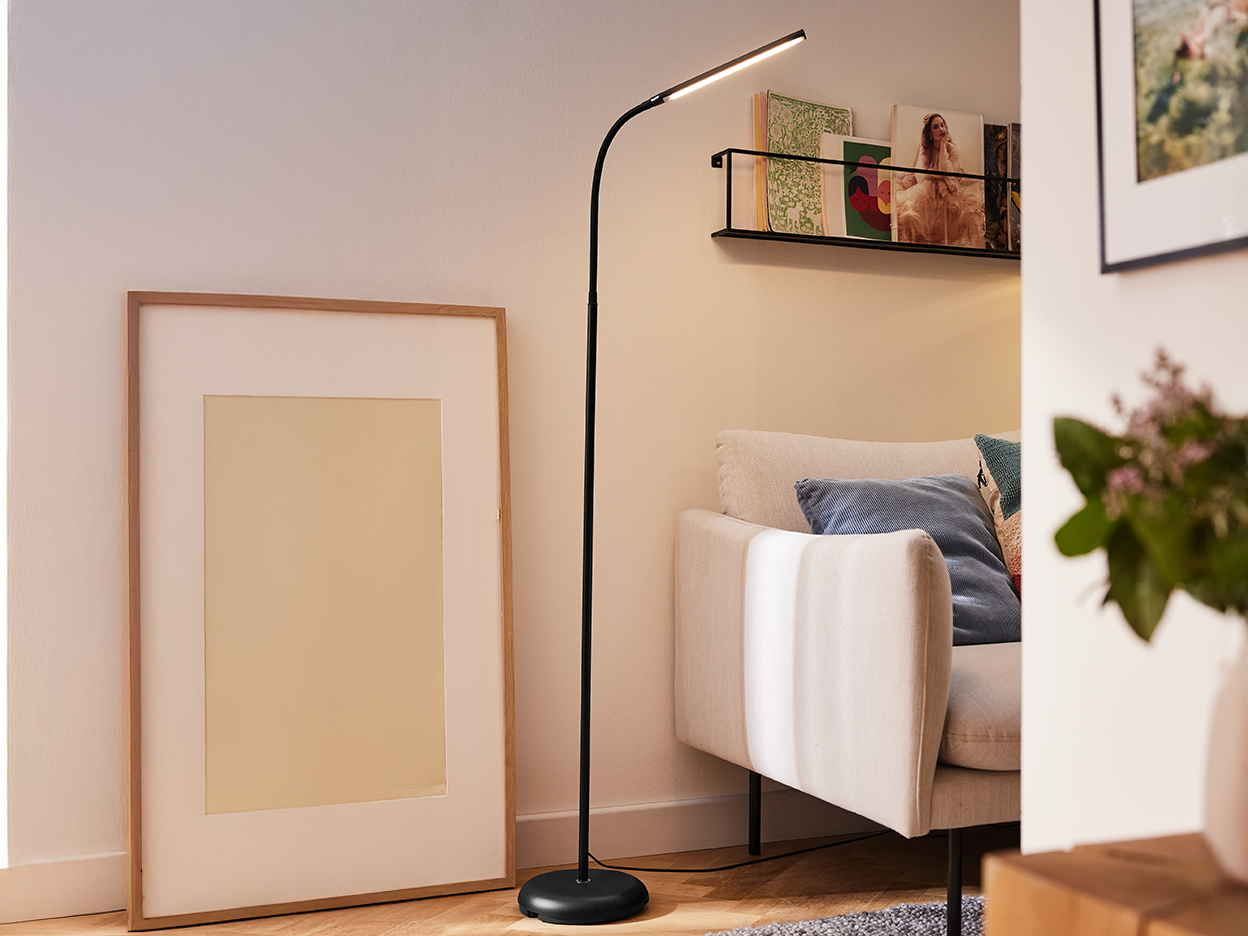 A modern black floor lamp illuminates a living room with a beige sofa and framed art.