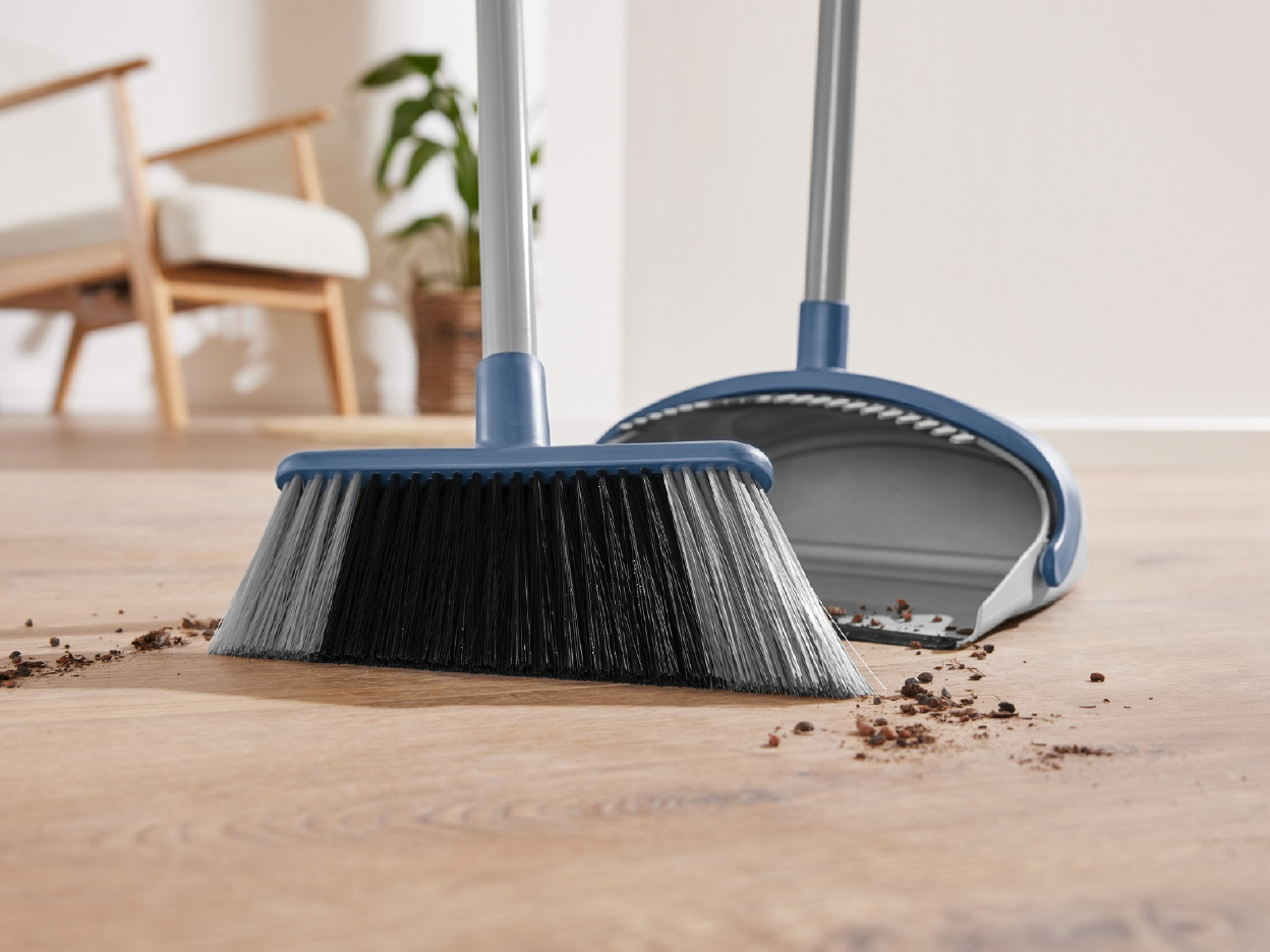 A broom and dustpan sweeping dirt on a wooden floor.