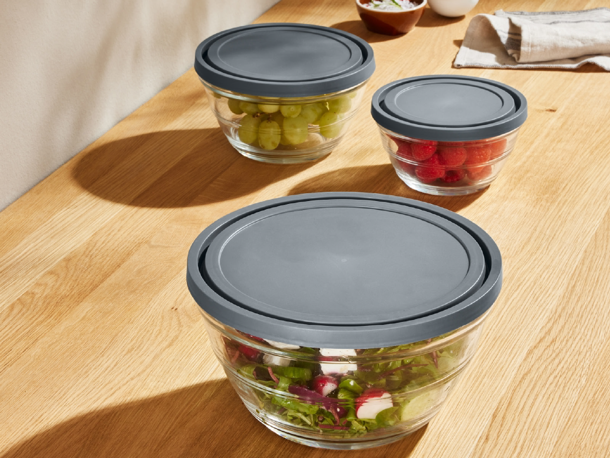 Three glass food storage containers with gray lids, filled with fruit and salad.