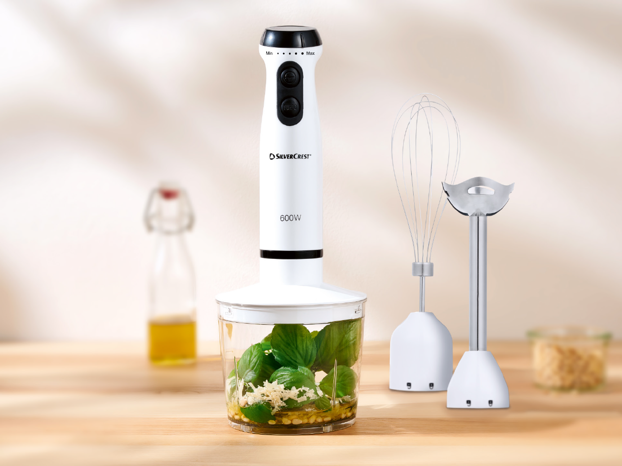SilverCrest hand blender with attachments and ingredients for pesto on a wooden table.