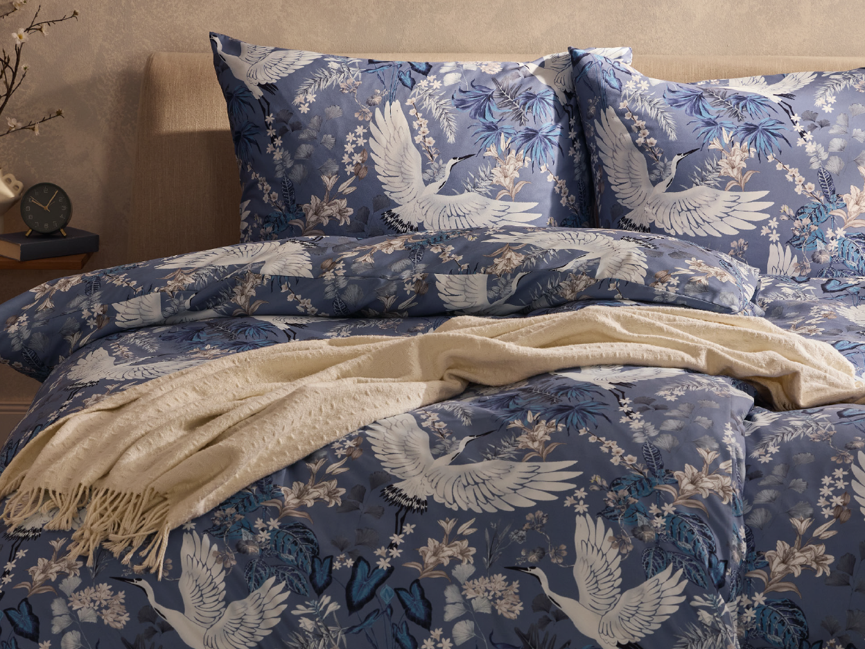 Blue duvet cover and pillowcases with white crane and floral patterns on a bed.