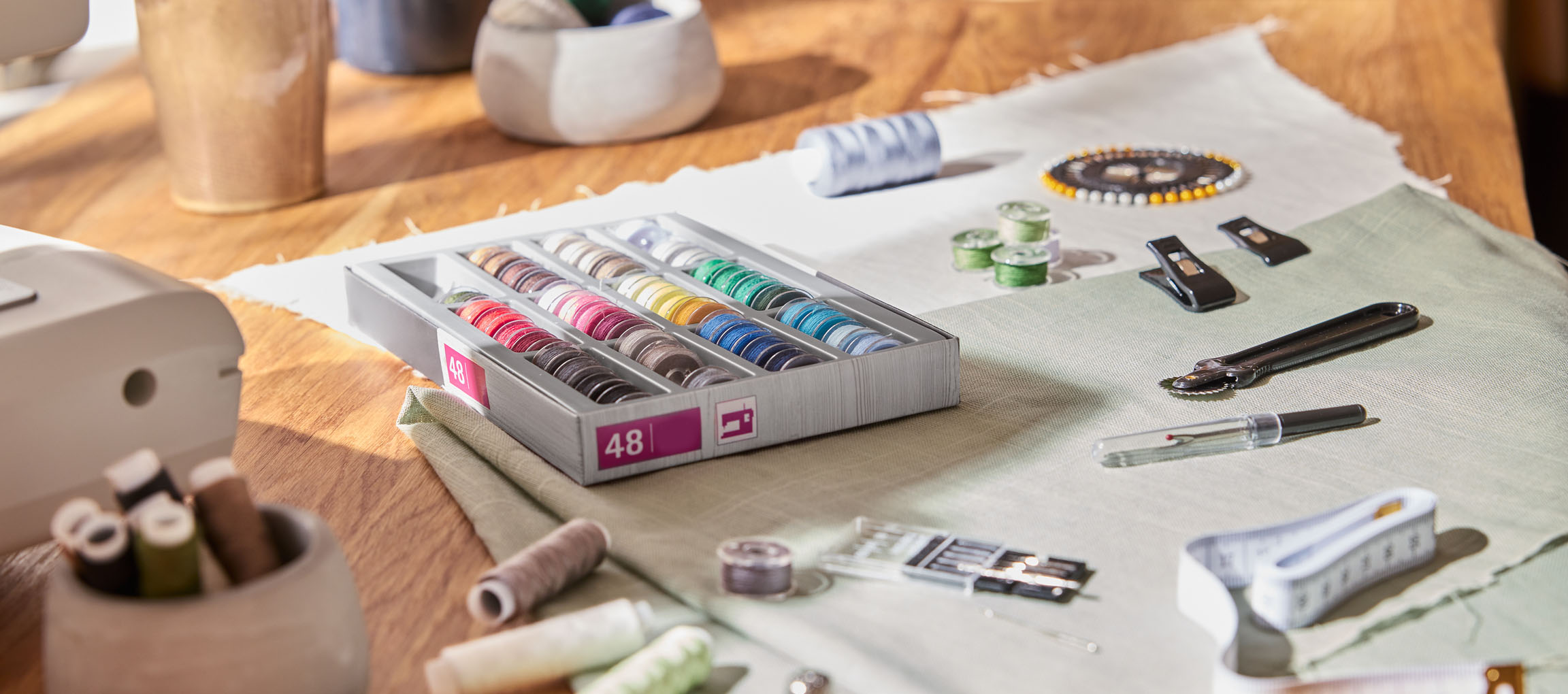 Είδη ραπτικής σε ξύλινο τραπέζι, συμπεριλαμβανομένου ενός οργανωτή κλωστών με 48 μπομπίνες, υφάσματος και διαφόρων εργαλείων.