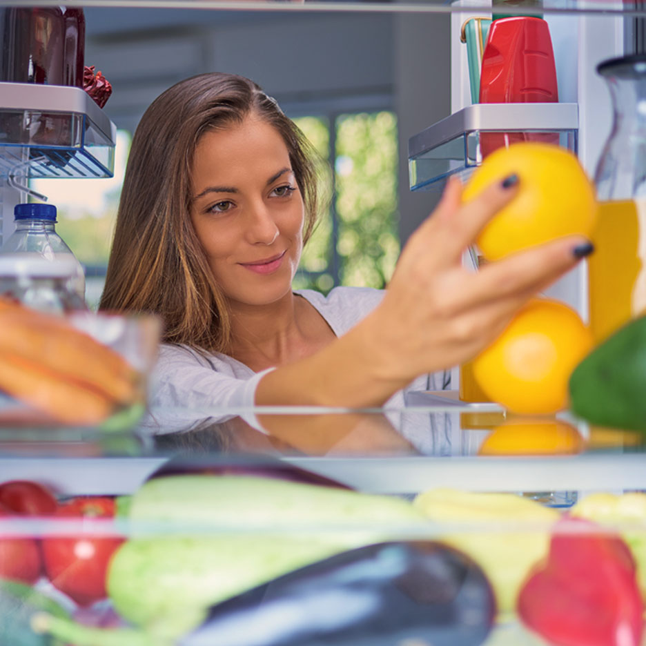 A woman reaches into a refrigerator to grab some oranges.