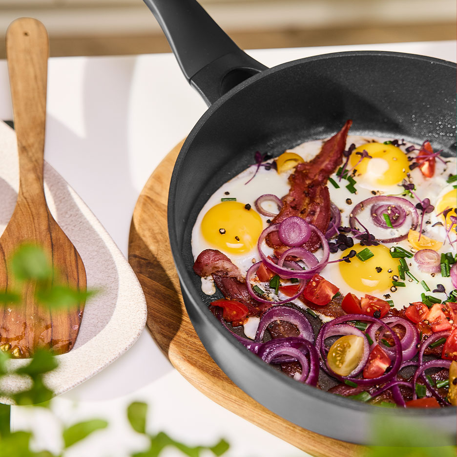 Frying pan with fried eggs, bacon, red onion, and tomatoes.